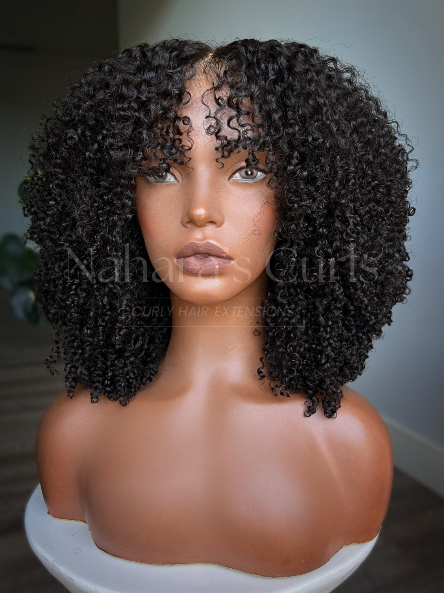 Centered view of natural curly human hair wig with full bangs and medium length curls
