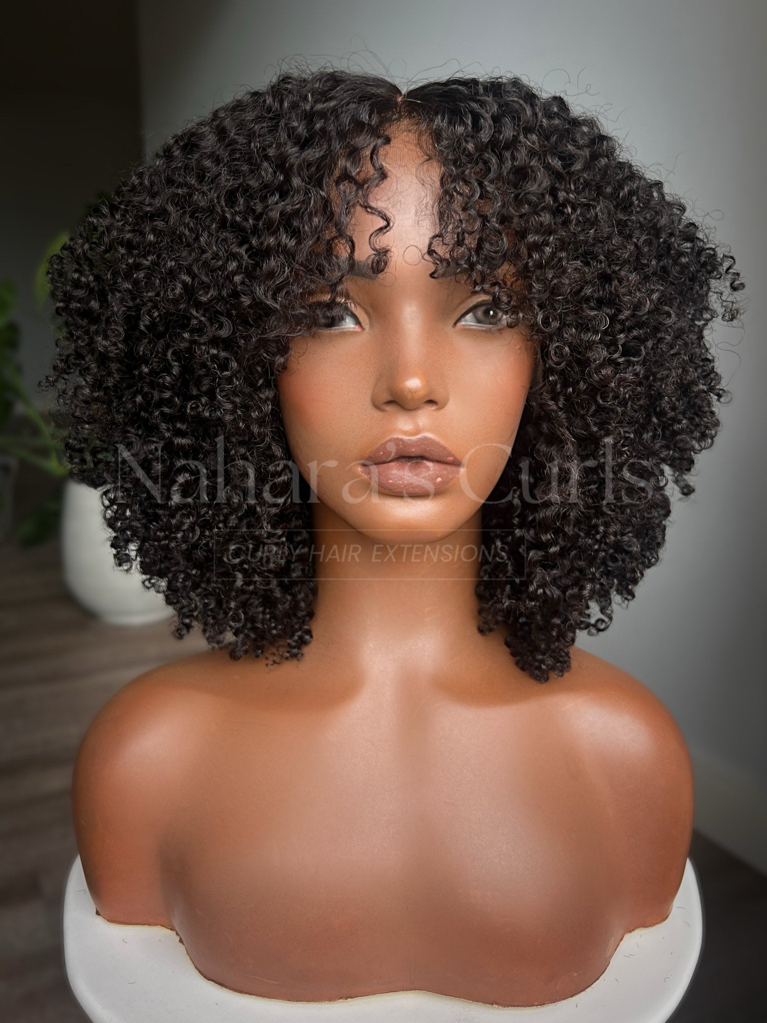 Mannequin head with curly hair extensions on a plain background